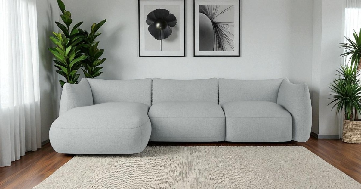 Bright modern living room with a light grey corner sofa, neutral rug, wooden floor, indoor plants and minimalist black-and-white wall art creating a calm contemporary interior.