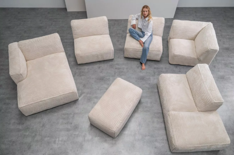 Beige modular corduroy sofa set with multiple seating sections and an ottoman arranged on a grey floor, with a woman sitting on one of the modules. Pastel Perfection for Contemporary Living Spaces