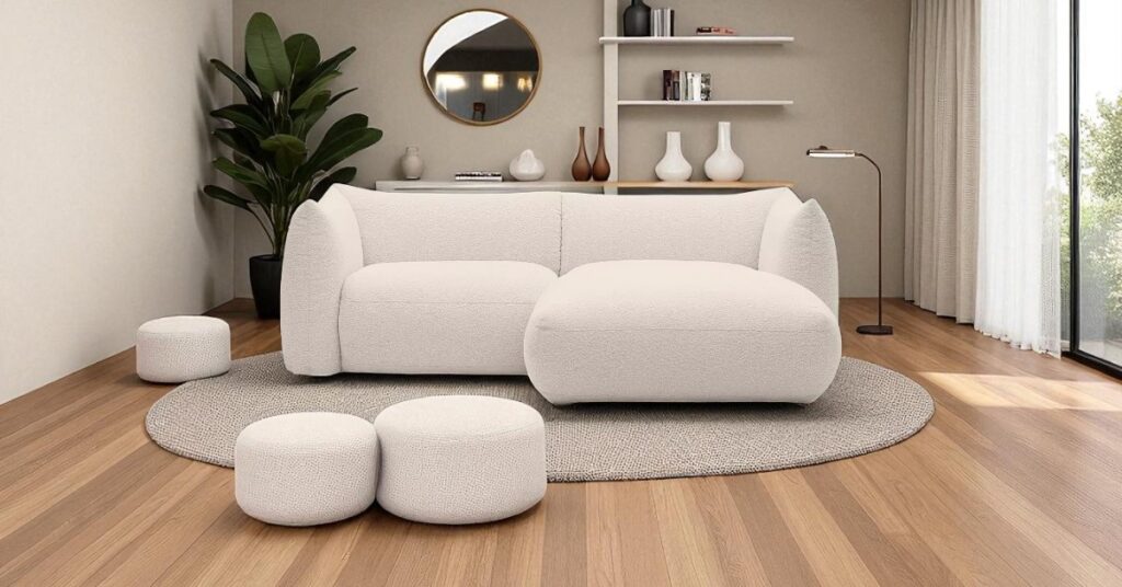Curved bouclé corner sofa in beige styled in a modern living room with round rug, pouffes, floor lamp and open shelving – curved furniture trend UK. Cosy Sofa